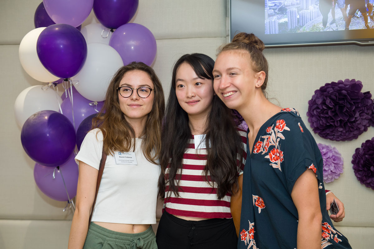 Three HKBU students smile and pose in front of purple and white balloons and purple flower decor