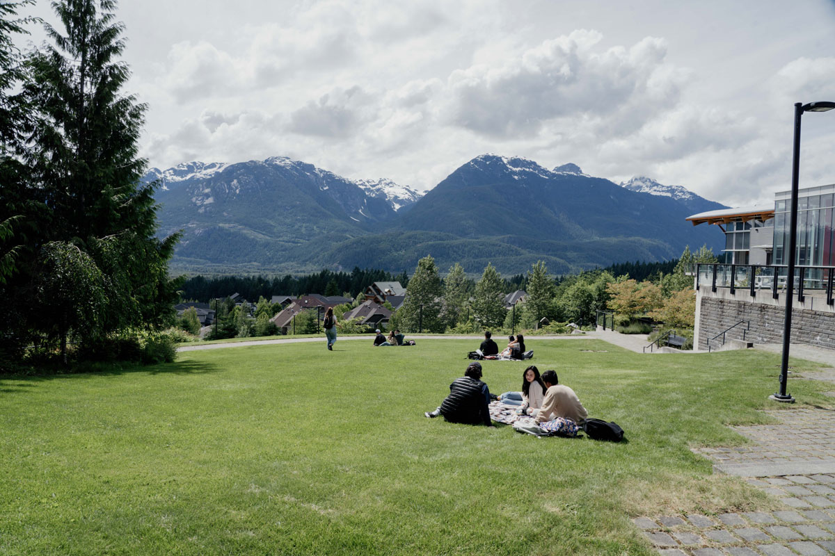 Quest University Canada students sit on a grassy lawn overlooking snowcapped mountains in the distance